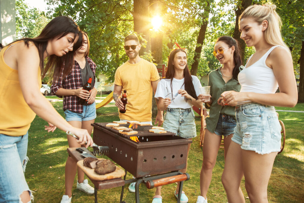 Groupe d'amis joyeux profitant d'une fête en plein air avec des bières et un barbecue par une journée ensoleillée.